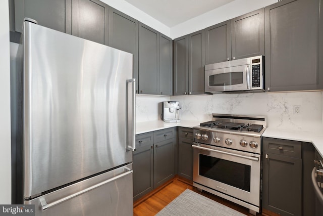 kitchen featuring light wood finished floors, tasteful backsplash, light countertops, gray cabinetry, and appliances with stainless steel finishes