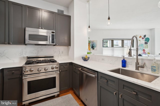 kitchen with light stone counters, stainless steel appliances, a sink, hanging light fixtures, and backsplash