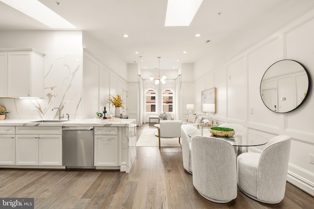 kitchen with stainless steel dishwasher, a decorative wall, a sink, and a skylight