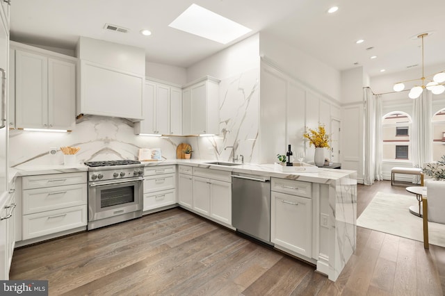 kitchen featuring tasteful backsplash, white cabinetry, a skylight, appliances with stainless steel finishes, and wood finished floors