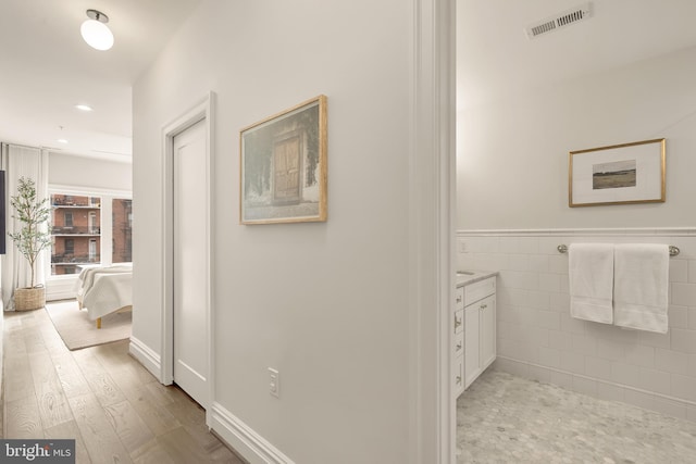hall with visible vents, recessed lighting, wainscoting, tile walls, and light wood finished floors
