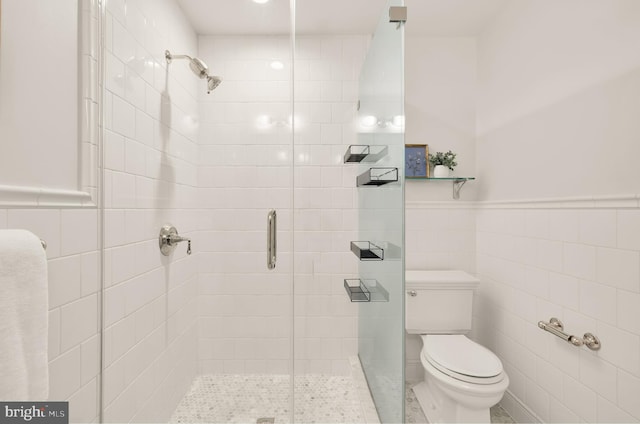 bathroom featuring toilet, wainscoting, tile walls, and a stall shower