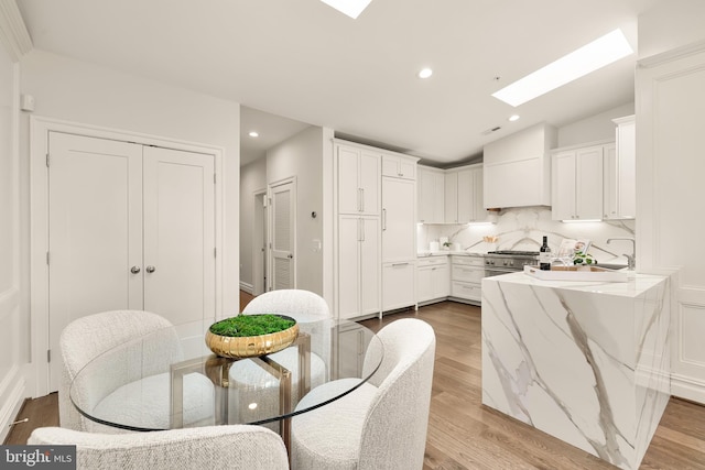 dining area with recessed lighting, vaulted ceiling with skylight, and light wood finished floors