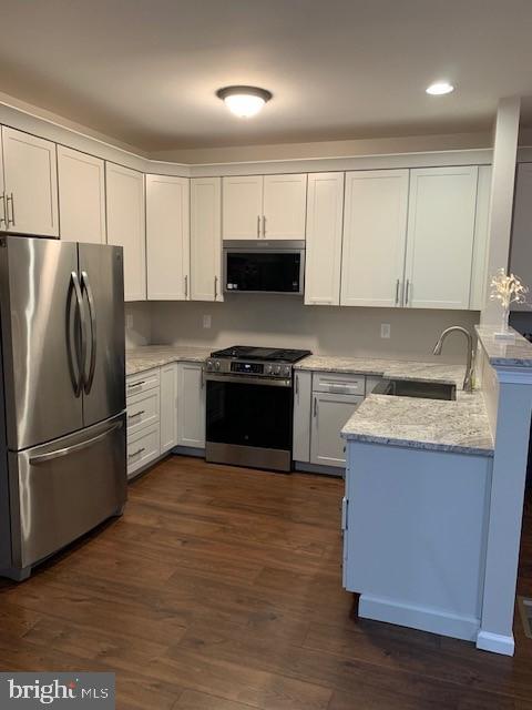 kitchen featuring light stone counters, dark wood-type flooring, a sink, white cabinetry, and appliances with stainless steel finishes