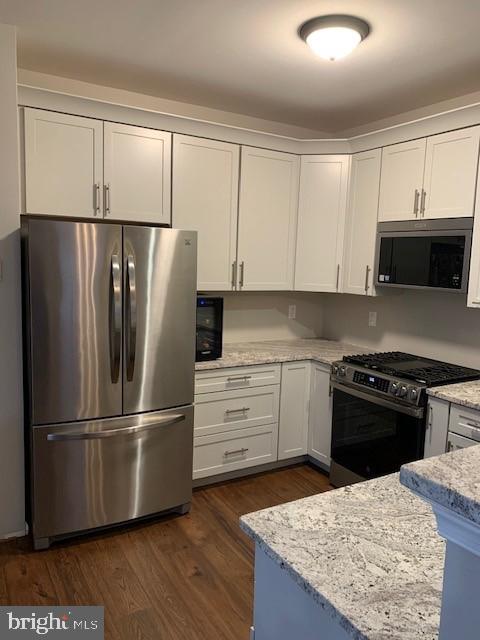 kitchen featuring dark wood-style floors, appliances with stainless steel finishes, white cabinets, and light stone counters