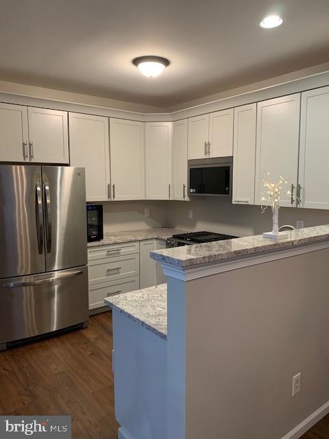 kitchen featuring light stone counters, dark wood-style floors, stainless steel appliances, white cabinetry, and a peninsula