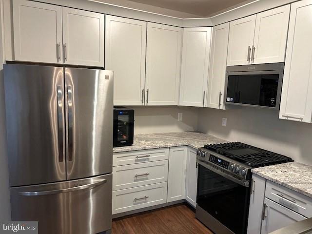 kitchen featuring stainless steel appliances, dark wood-type flooring, light stone counters, and white cabinetry