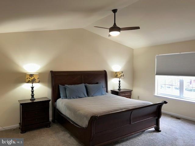 carpeted bedroom featuring visible vents, baseboards, vaulted ceiling, and a ceiling fan