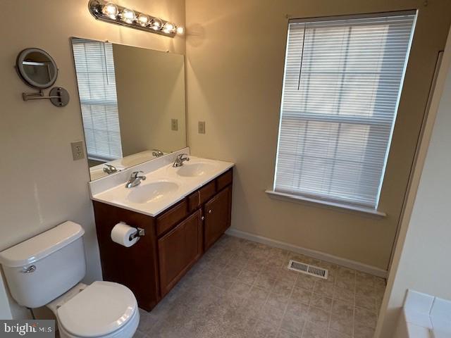 full bathroom featuring visible vents, a sink, toilet, and double vanity