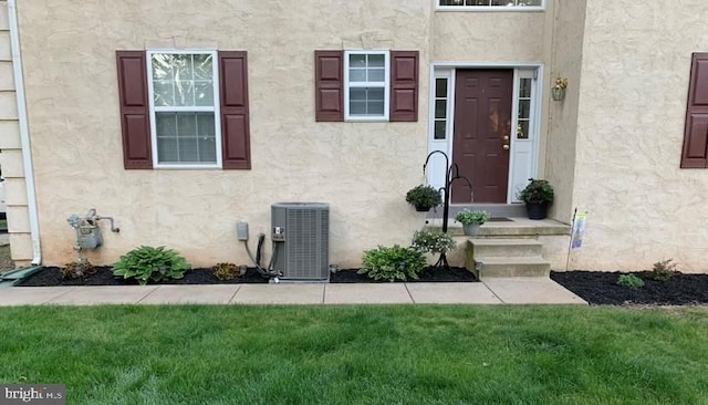 property entrance featuring central air condition unit, a lawn, and stucco siding