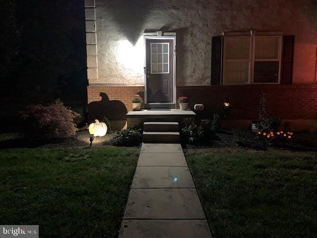 entrance to property with brick siding and a lawn