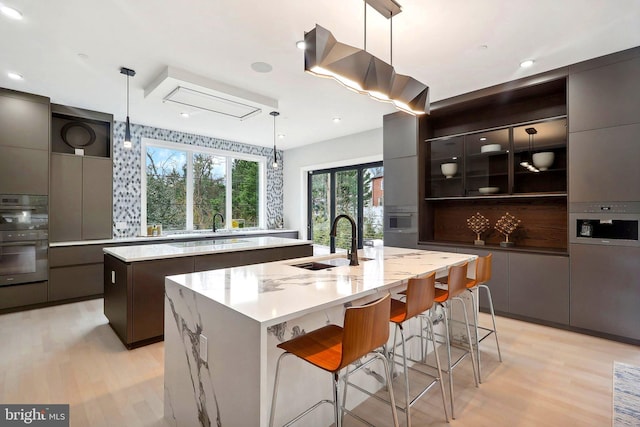 kitchen featuring modern cabinets, a center island with sink, a sink, and open shelves