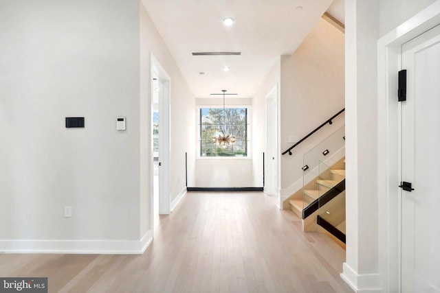 foyer featuring light wood-type flooring, a notable chandelier, stairway, and baseboards