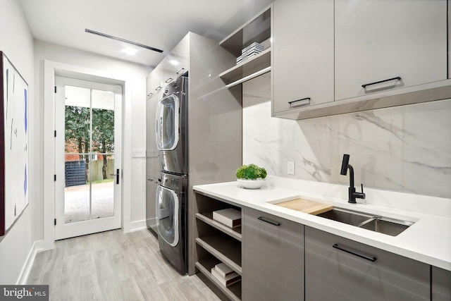 washroom featuring stacked washer and clothes dryer, cabinet space, a sink, and light wood finished floors