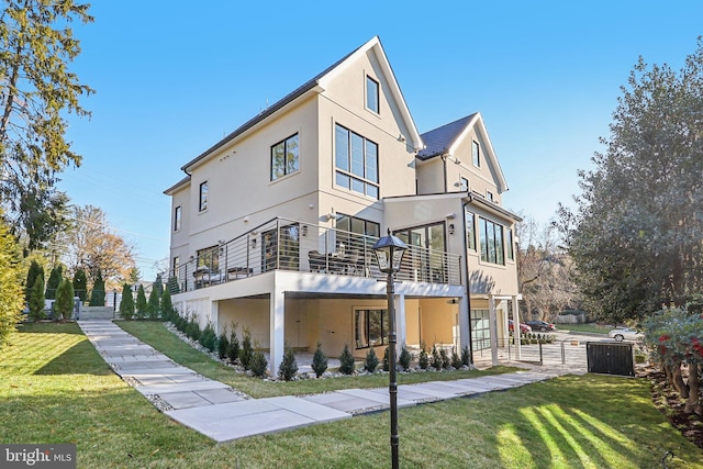 back of house featuring a lawn, fence, a balcony, and stucco siding