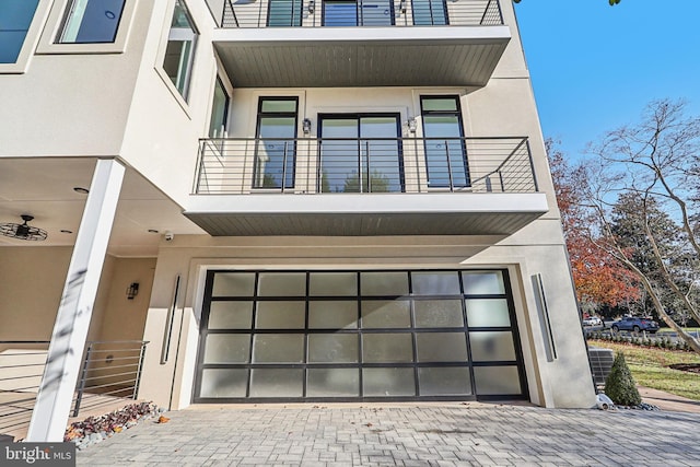 exterior space with decorative driveway, an attached garage, a balcony, and stucco siding