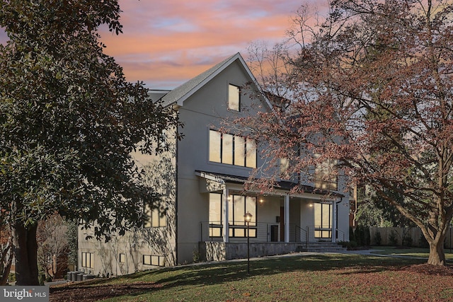 view of front facade featuring a lawn, fence, a porch, central AC, and stucco siding