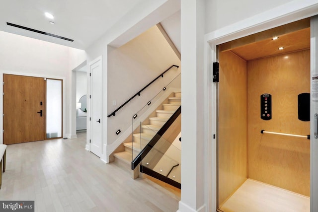 stairs featuring elevator and wood finished floors