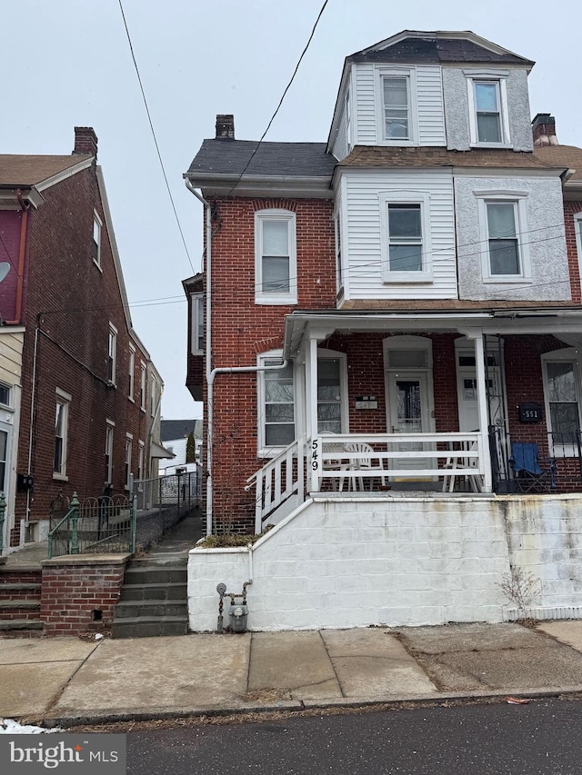 townhome / multi-family property featuring covered porch and brick siding