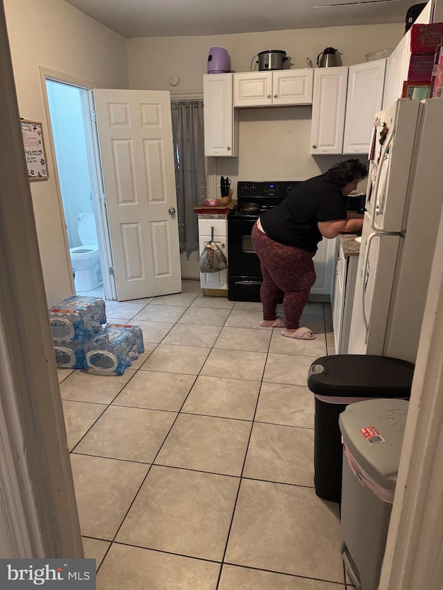 kitchen with white cabinets, light tile patterned flooring, freestanding refrigerator, and black electric range oven