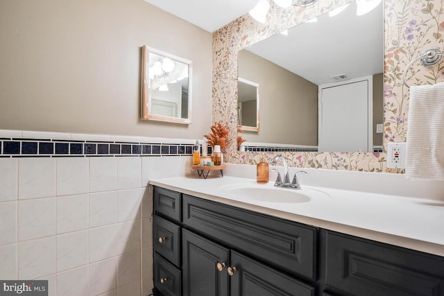 bathroom with tile walls, visible vents, wainscoting, vanity, and wallpapered walls