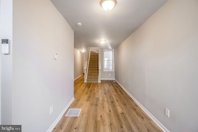 hallway featuring visible vents, baseboards, light wood-style flooring, and stairway