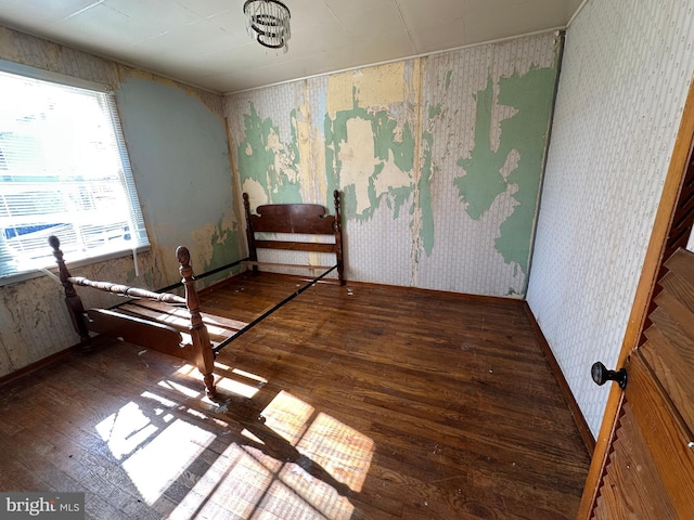 unfurnished bedroom featuring baseboards, hardwood / wood-style floors, and wallpapered walls