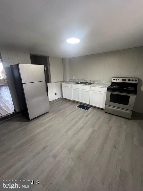 kitchen with light wood finished floors, stainless steel appliances, light countertops, white cabinets, and a sink