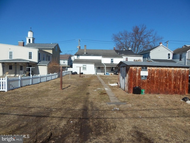 rear view of property featuring an outdoor structure, fence, and a residential view