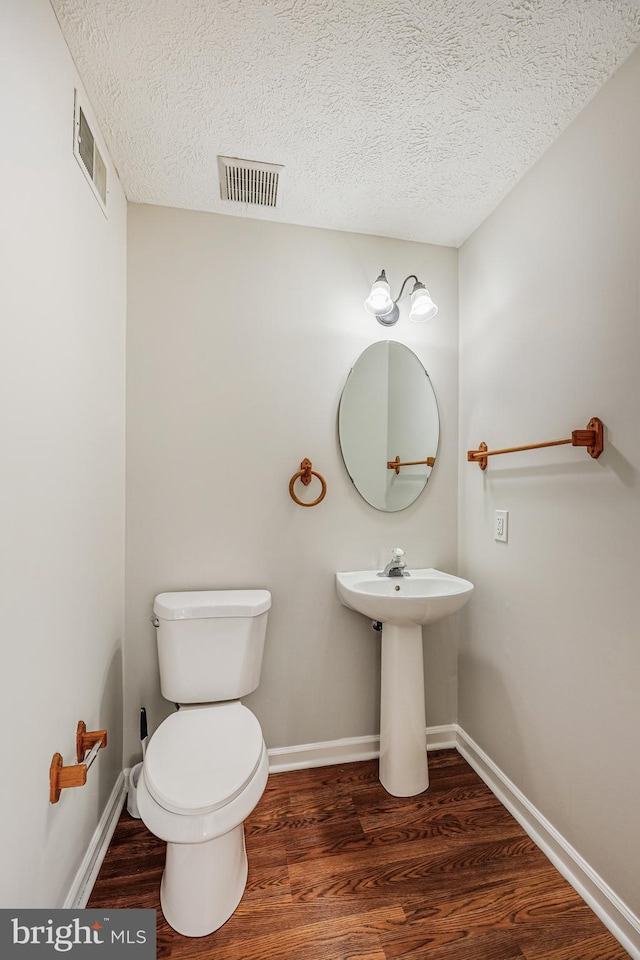 half bath featuring visible vents, a textured ceiling, and wood finished floors