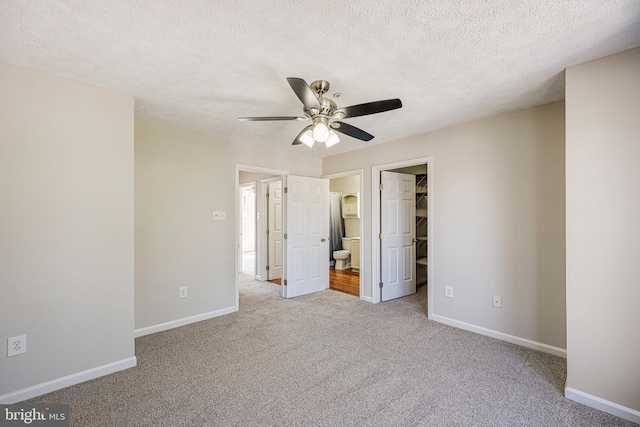 unfurnished bedroom featuring a spacious closet, baseboards, carpet floors, a closet, and a textured ceiling