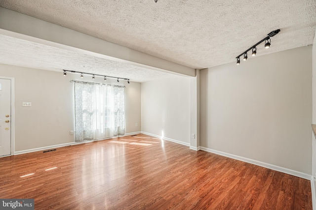 spare room with rail lighting, a textured ceiling, baseboards, and wood finished floors