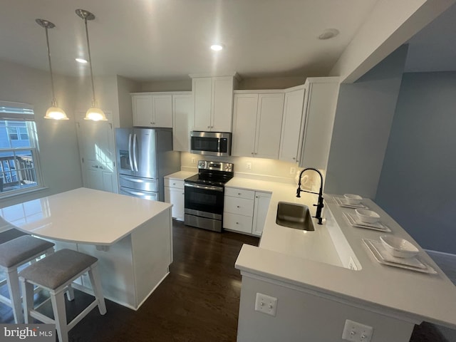 kitchen featuring a breakfast bar area, dark wood-style flooring, a sink, light countertops, and appliances with stainless steel finishes