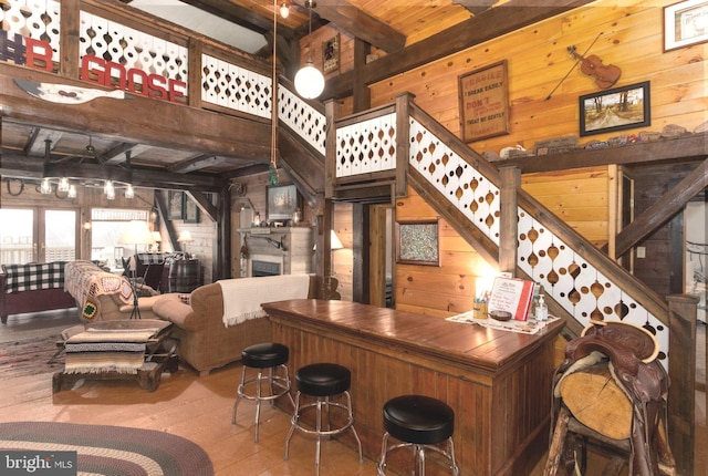 bar featuring a dry bar, beamed ceiling, stairs, wood walls, and a fireplace