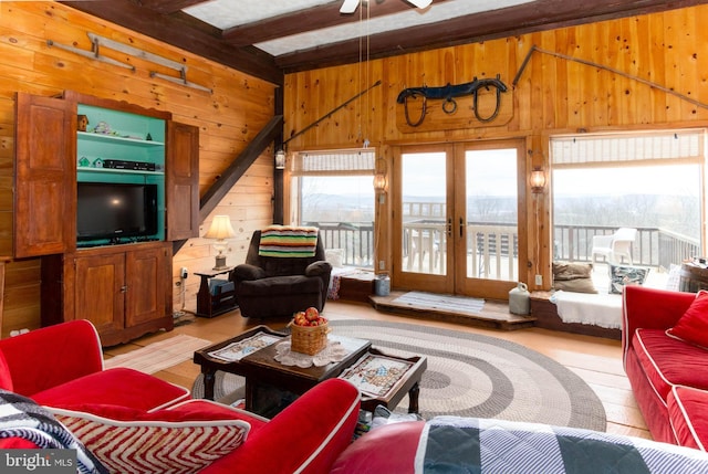 living room featuring beamed ceiling, french doors, wood walls, and a wealth of natural light