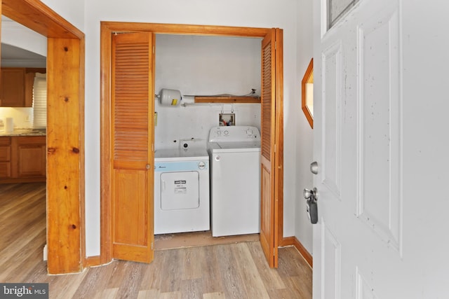 clothes washing area with laundry area, washer and clothes dryer, light wood-type flooring, and baseboards