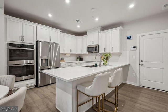 kitchen with a breakfast bar area, stainless steel appliances, visible vents, a sink, and a peninsula