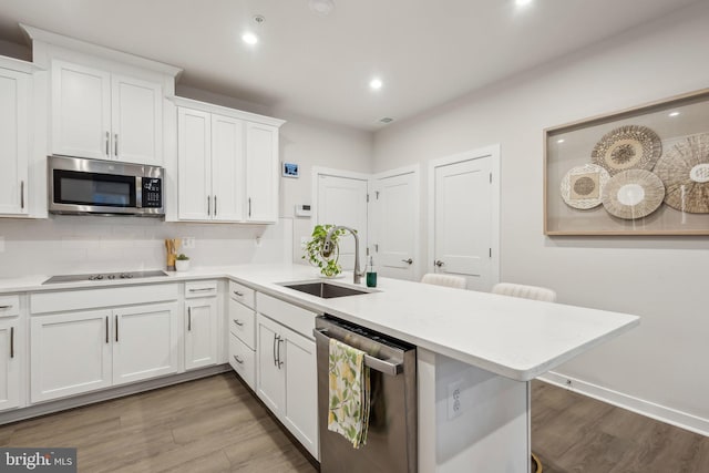 kitchen with light countertops, appliances with stainless steel finishes, a sink, wood finished floors, and a peninsula