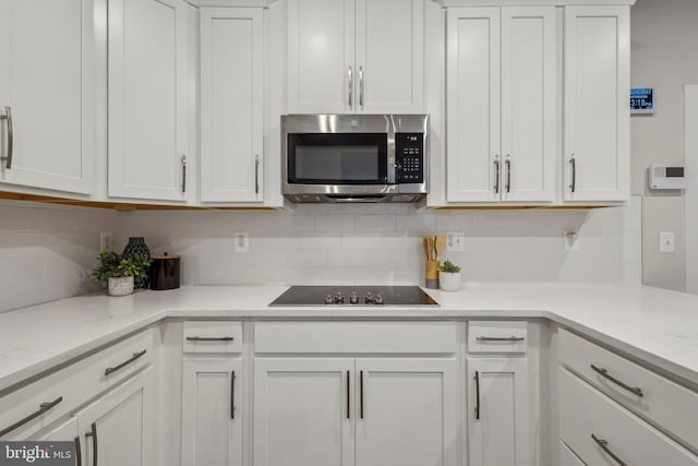 kitchen featuring tasteful backsplash, stainless steel microwave, black electric stovetop, and white cabinetry