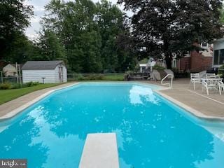 pool featuring a diving board, a storage unit, an outdoor structure, and a patio area