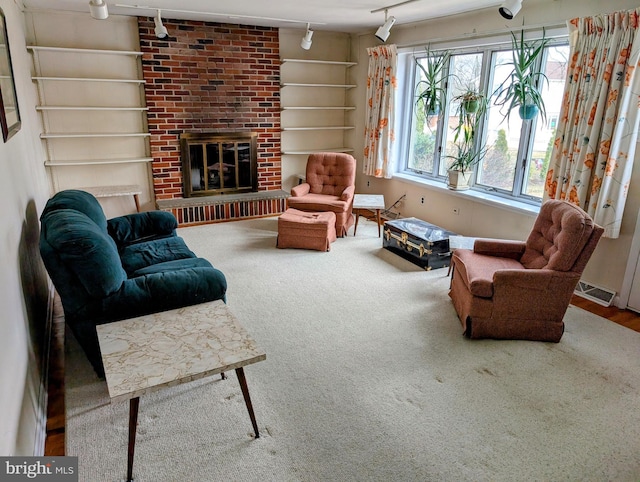 living room with built in shelves, visible vents, carpet floors, track lighting, and a brick fireplace