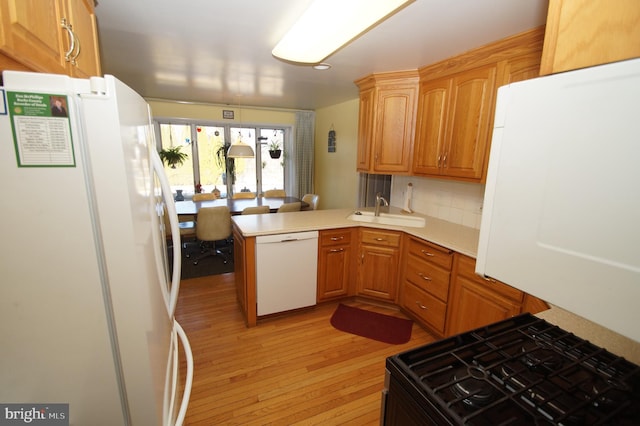 kitchen featuring white appliances, a peninsula, a sink, light countertops, and light wood-style floors