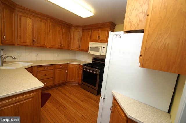 kitchen with white microwave, stainless steel range with gas cooktop, light countertops, brown cabinetry, and a sink