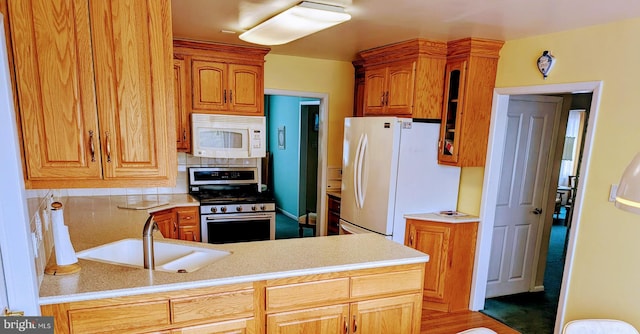 kitchen featuring decorative backsplash, white appliances, light countertops, and a sink