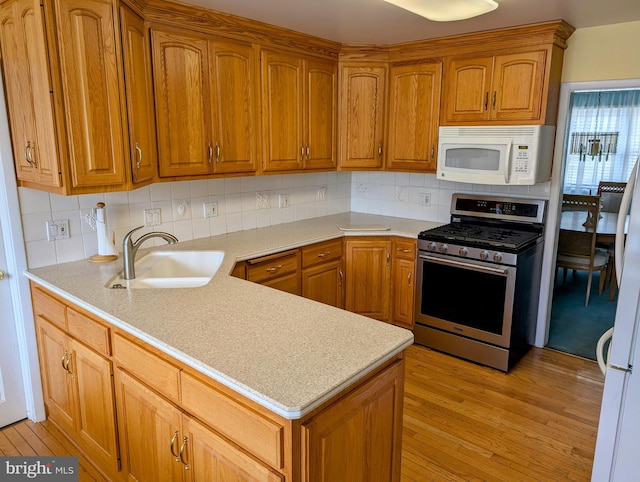 kitchen with white microwave, stainless steel range with gas stovetop, light countertops, decorative backsplash, and a sink