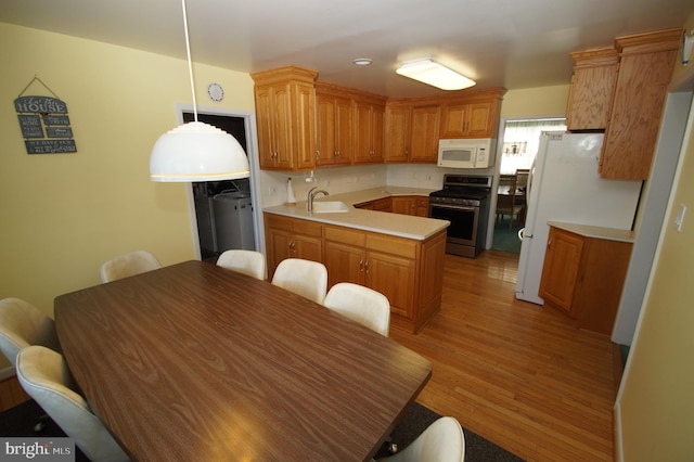 kitchen with light wood finished floors, a sink, white appliances, a peninsula, and light countertops