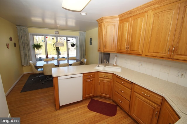 kitchen featuring dishwasher, a peninsula, light wood-style flooring, and a sink