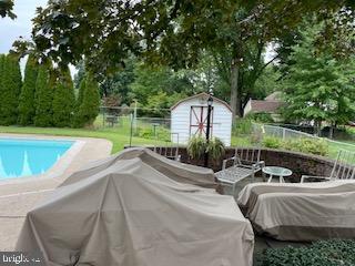 outdoor pool with a storage shed, fence, an outdoor living space, and an outdoor structure