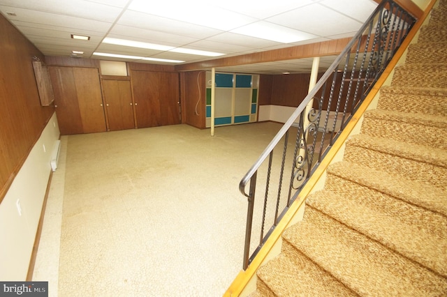 finished basement featuring a drop ceiling, wood walls, and stairs