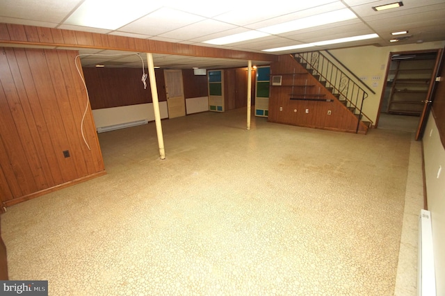 finished basement with wooden walls, stairway, visible vents, and a drop ceiling